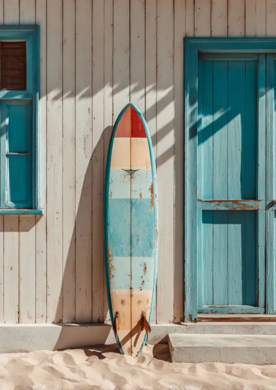 Vintage verweerde gestreepte surfplank in blauw crème en koraalrood leunend tegen een witgekalkt houten strandhuisje met turquoise deur en raam op wit zand met palmboomschaduwen